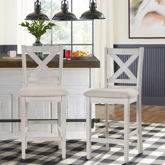Two gray and white solid sheesham wood cross bar chairs with cushioned seats and backrests, standing in a kitchen setting with a counter and hanging lights in the background.