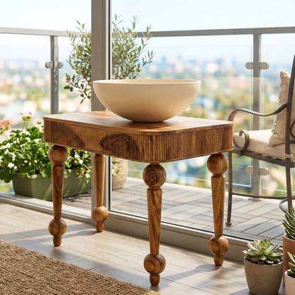 Wooden side table with a bowl on a patio with plants and a chair.