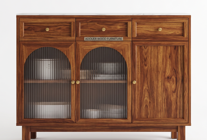 A wooden sideboard cabinet with a rich brown wood grain finish, featuring three drawers on top, two arched glass-front doors with vertical ribbed glass panels, and a right-side solid wood door. Small brass knobs are used for handles, and a metal sign on the front reads 'ADOUER WOOD FURNITURE'.