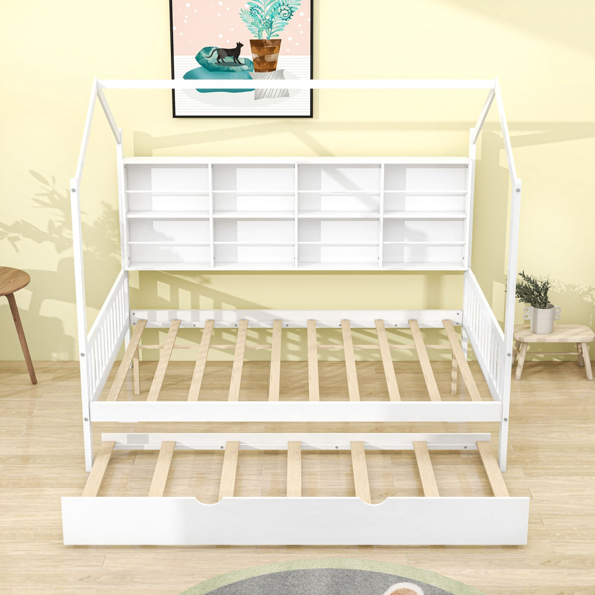 White children's bed with wooden slats in a room with a yellow wall and a small table.