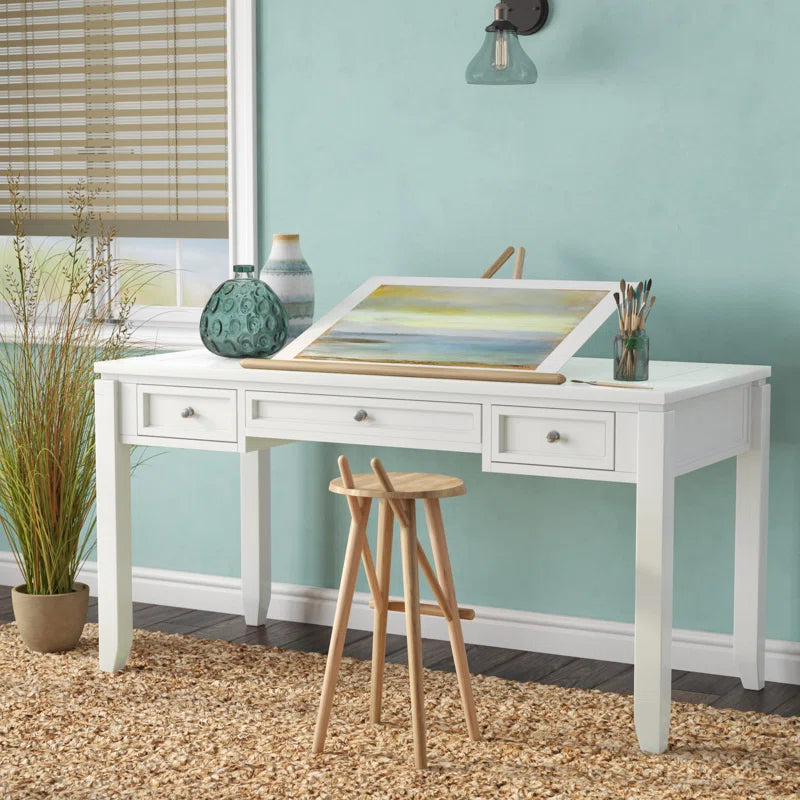 White finished solid Sheesham wood 3-drawer study and office table with metal frame, accompanied by a wooden stool and decorative items. The table has an open drawer and is placed in a room with a light blue wall and a potted plant.
