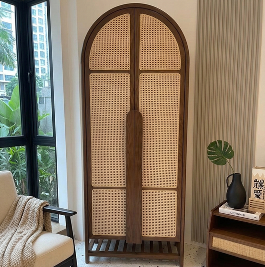 Wooden arched cabinet with wicker design in a room with a chair and small table.