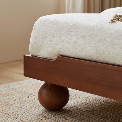 Wooden bed frame with spherical legs on a carpeted floor.