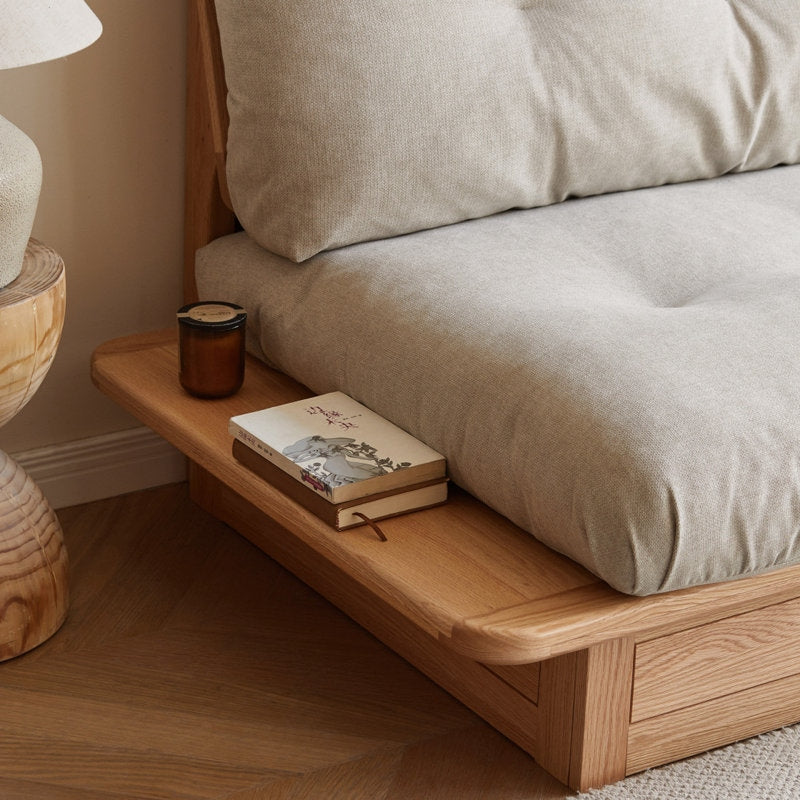 Wooden bedside table with books and a candle next to a sofa with beige cushions.