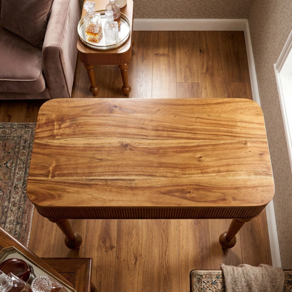 Wooden coffee table in a living room setting with a couch and side table in the background.