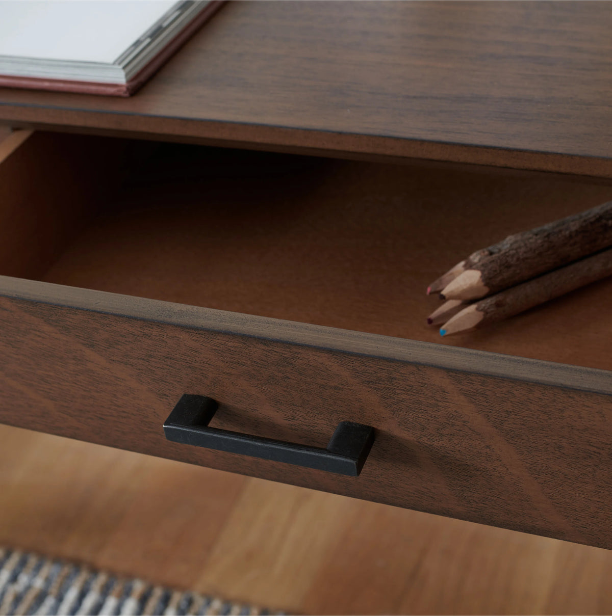 Wooden drawer with a black handle and pencils on top