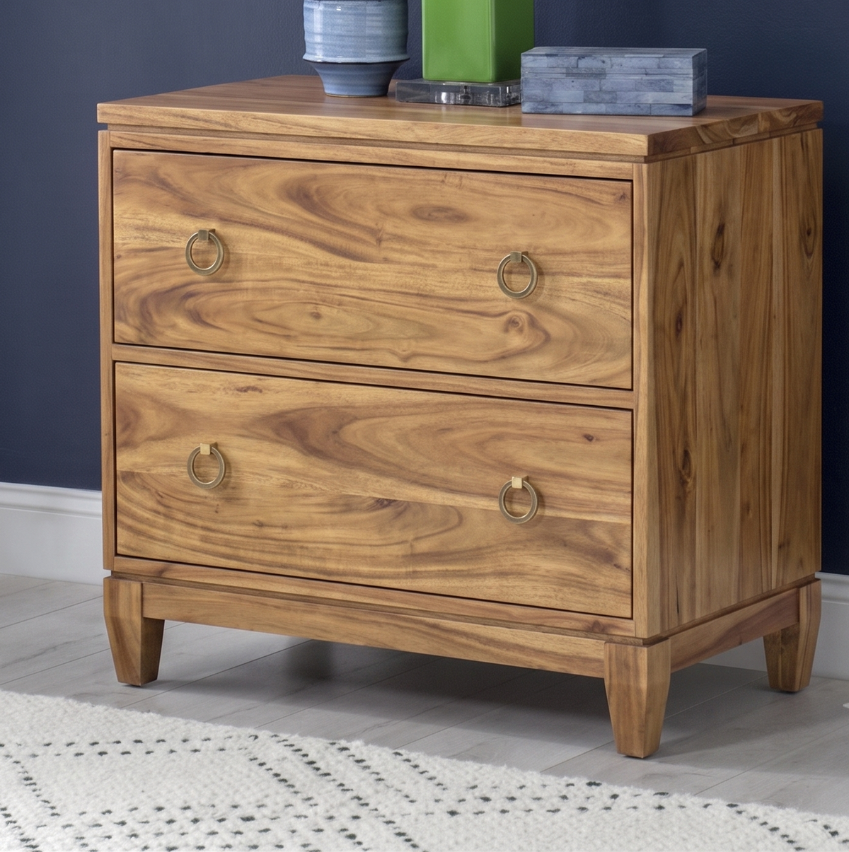 Wooden dresser with two drawers on a gray floor against a dark blue wall.