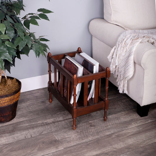 Wooden magazine rack with magazines on a wooden floor next to a plant and a sofa.