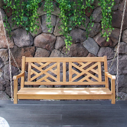 Wooden swing bench with lattice design against a stone wall with greenery