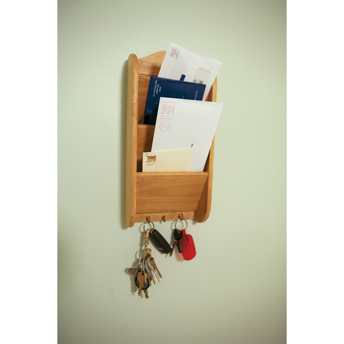 Wooden wall-mounted organizer with keys and mail on a light green wall