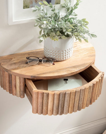 Wooden wall-mounted shelf with a plant, glasses, and a box on a white wall.