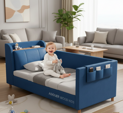 Child sitting on a blue children's bed in a living room with gray sofas and a plant.