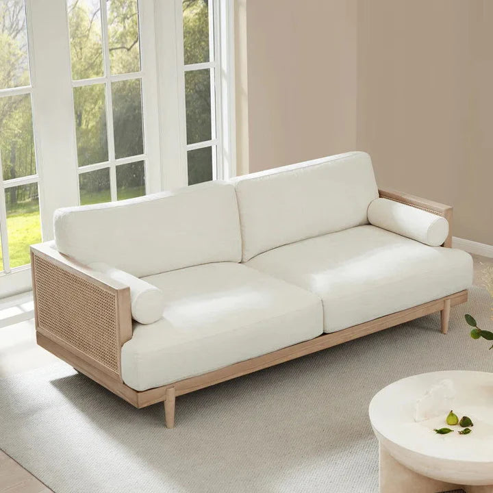 A cream upholstered three-seater sofa with solid wood cane frame, positioned in a well-lit room with a light color scheme.