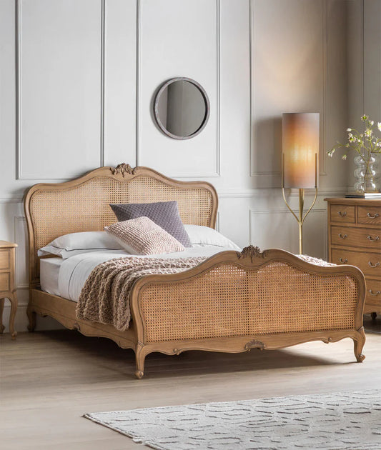 A luxurious French vintage rattan bed with a high headboard, made of sheesham wood, placed in a bedroom setting with decorative pillows, a blanket, and a wooden floor.
