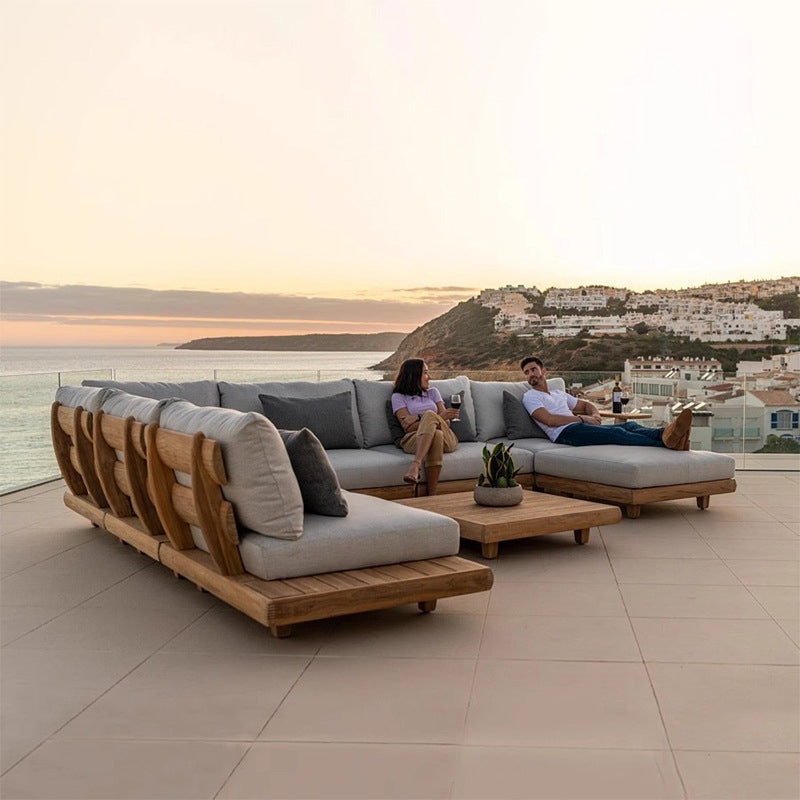 A luxurious solid acacia wood outdoor patio sofa set with fabric upholstery, arranged in a right-hand configuration with a coffee table, on a tiled floor with an ocean view in the background.