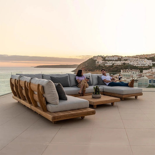 A luxurious solid acacia wood outdoor patio sofa set with fabric upholstery, arranged in a right-hand configuration with a coffee table, on a tiled floor with an ocean view in the background.