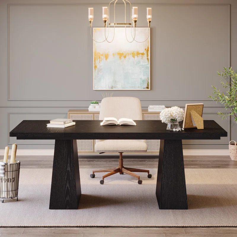 A modern black executive desk with trestle legs, shown in an elegantly furnished home office setting with a chair, decorative items, and wall art in the background.