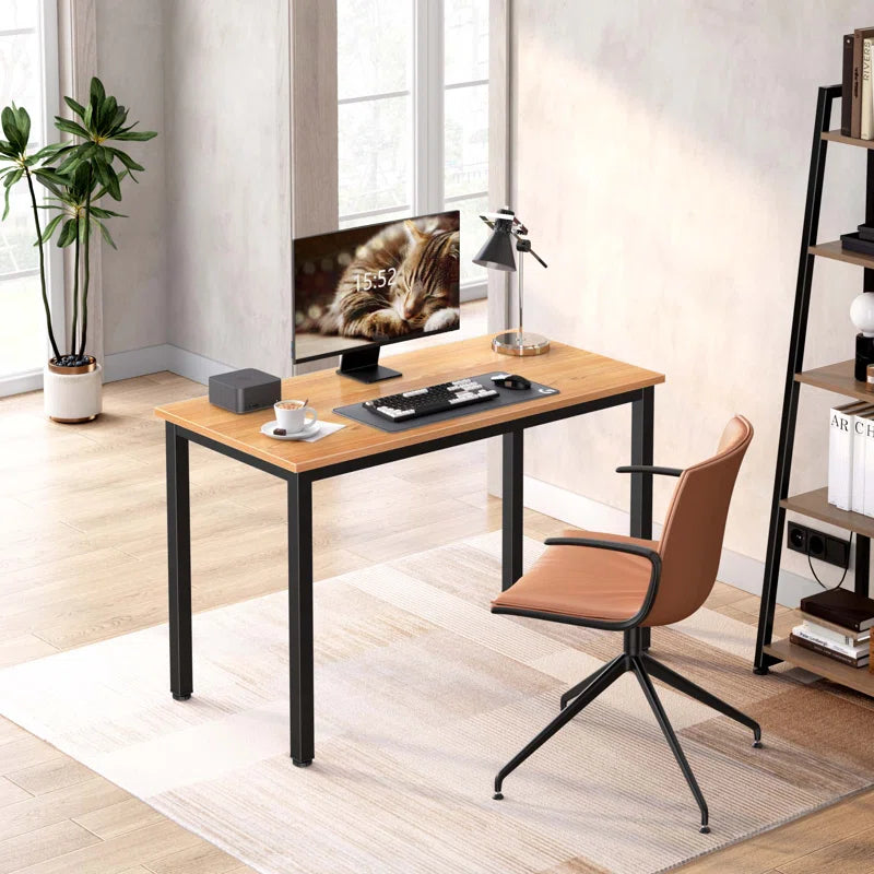 A modern computer desk with a office chair, set in an office environment with decorative items and a potted plant. The desk has a wooden tabletop and metal frame.
