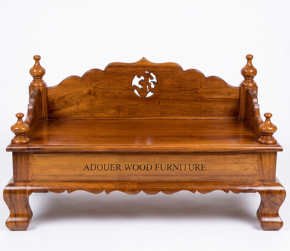 A polished reddish-brown wooden bench with ornate turned legs, a scalloped backrest, and a central cutout featuring a stylized figure. The front panel is engraved with the text 'ADOUER WOOD FURNITURE'.