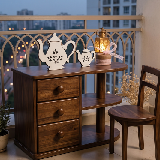 Wooden desk, chair with decorative teapots and a lit lantern on a balcony at night.