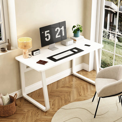 A white classic study table with round edges and a digital clock on top, placed in a room with a chair and a lamp.