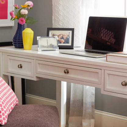 Desk with laptop, vase of flowers, and photo frame in a home office setting.