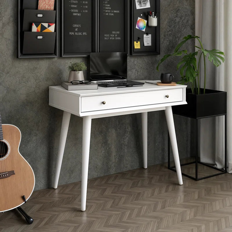 A white solid sheesham wood study desk with a drawer, featuring a modern design and supported by splayed legs, positioned in a room with a guitar and decorative items on it.