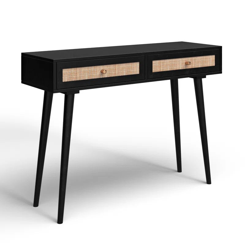 A wooden console table with drawers, featuring a lamp and a framed picture on top, set against a white panelled background.