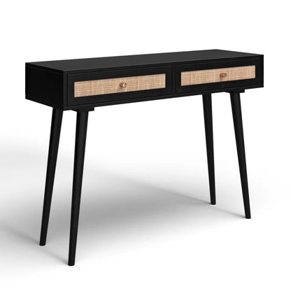 A wooden console table with drawers, featuring a lamp and a framed picture on top, set against a white panelled background.