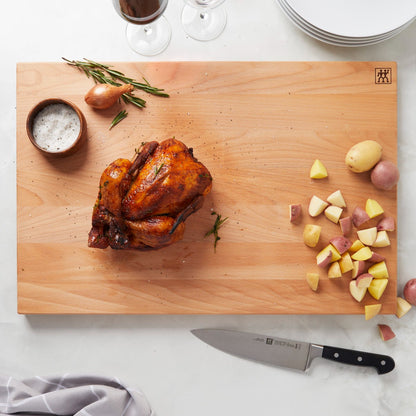 Roasted chicken on a wooden cutting board with potatoes and herbs, set on a marble surface.