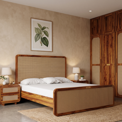 A wooden bed frame with a woven cane headboard and footboard, styled in a warm, modern bohemian bedroom with matching nightstands, a wooden wardrobe, and a framed botanical print on the wall.