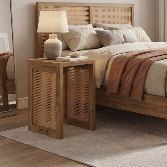 A wooden bedside table with woven cane panels and the brand name 'ADOUER WOOD ' printed on the front, styled next to a wooden bed in a warm, neutral-toned bedroom.