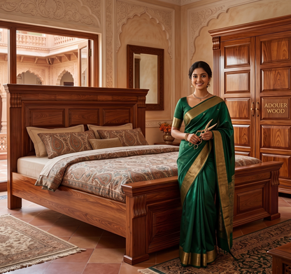 Woman in a green saree standing in a luxurious bedroom with wooden furniture.