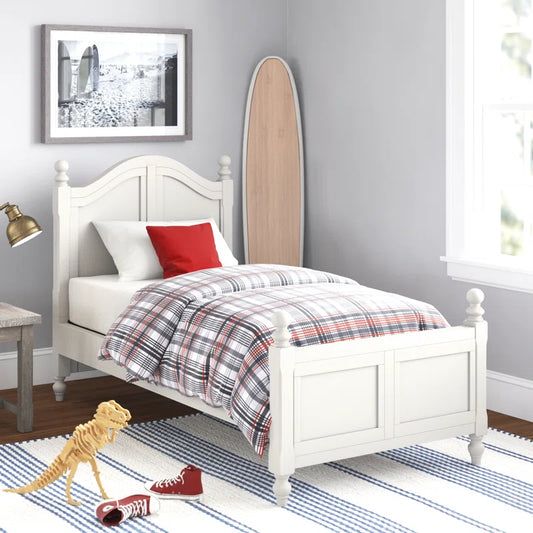 A white, solid sheesham wood classic bed for kids with a plaid mattress, placed in a bedroom setting with decorative items around it.