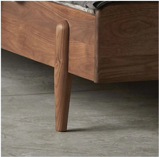 Close-up of a wooden bed frame showing the corner joint, side panel, and tapered leg on a gray concrete floor.