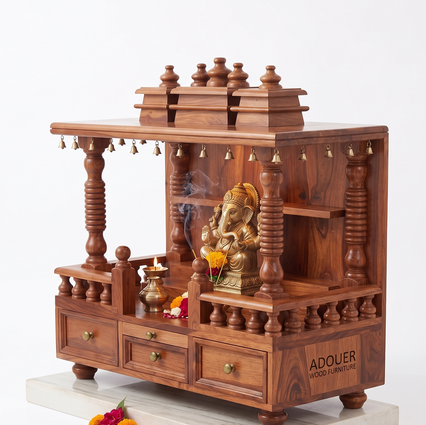 A wooden Ganesh idol display stand or miniature altar made of rich reddish-brown wood, featuring carved pillars, tiered shelves, small hanging bells, and three drawers. A brass Ganesh statue sits inside, with a diya and flowers arranged on and around it.