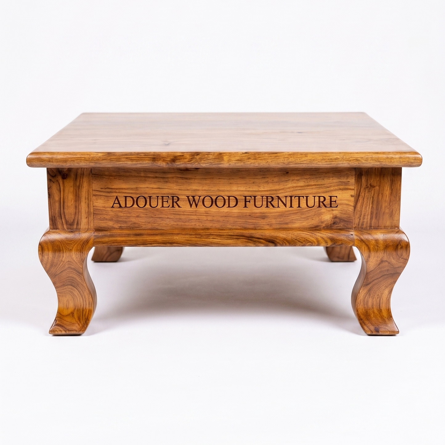 A square wooden pooja chowki with carved cabriole-style legs and a rich medium-brown wood grain finish, featuring the text 'ADOUER WOOD FURNITURE' engraved on the front panel, set against a plain white background.
